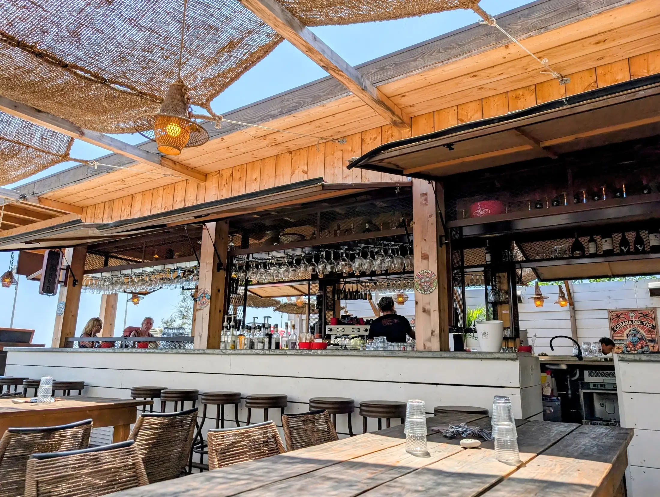 Le bar du restaurant : comptoir en bois clair et verres suspendus